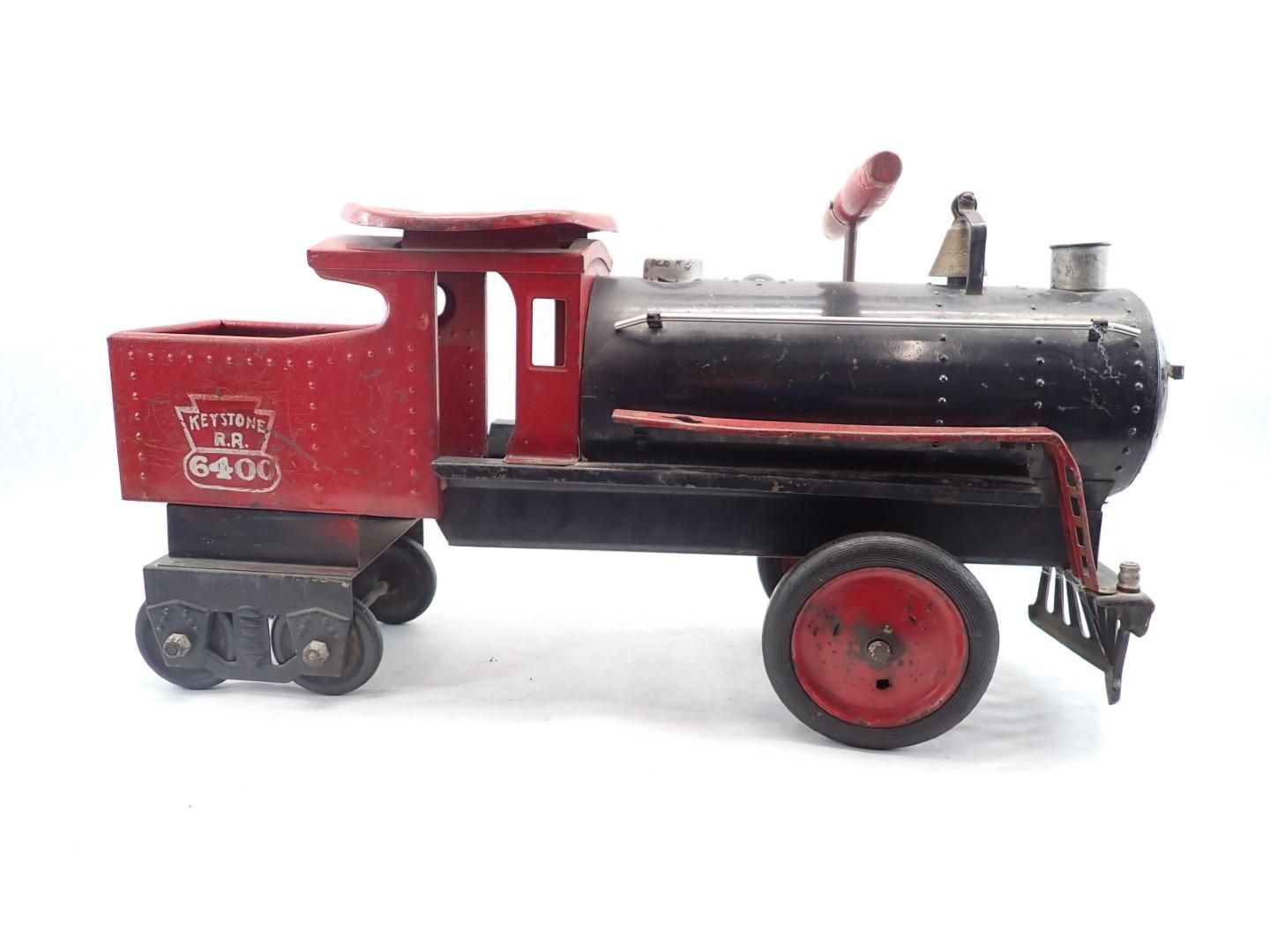 Red and black vintage toy train with wheels, sitting on a white surface.