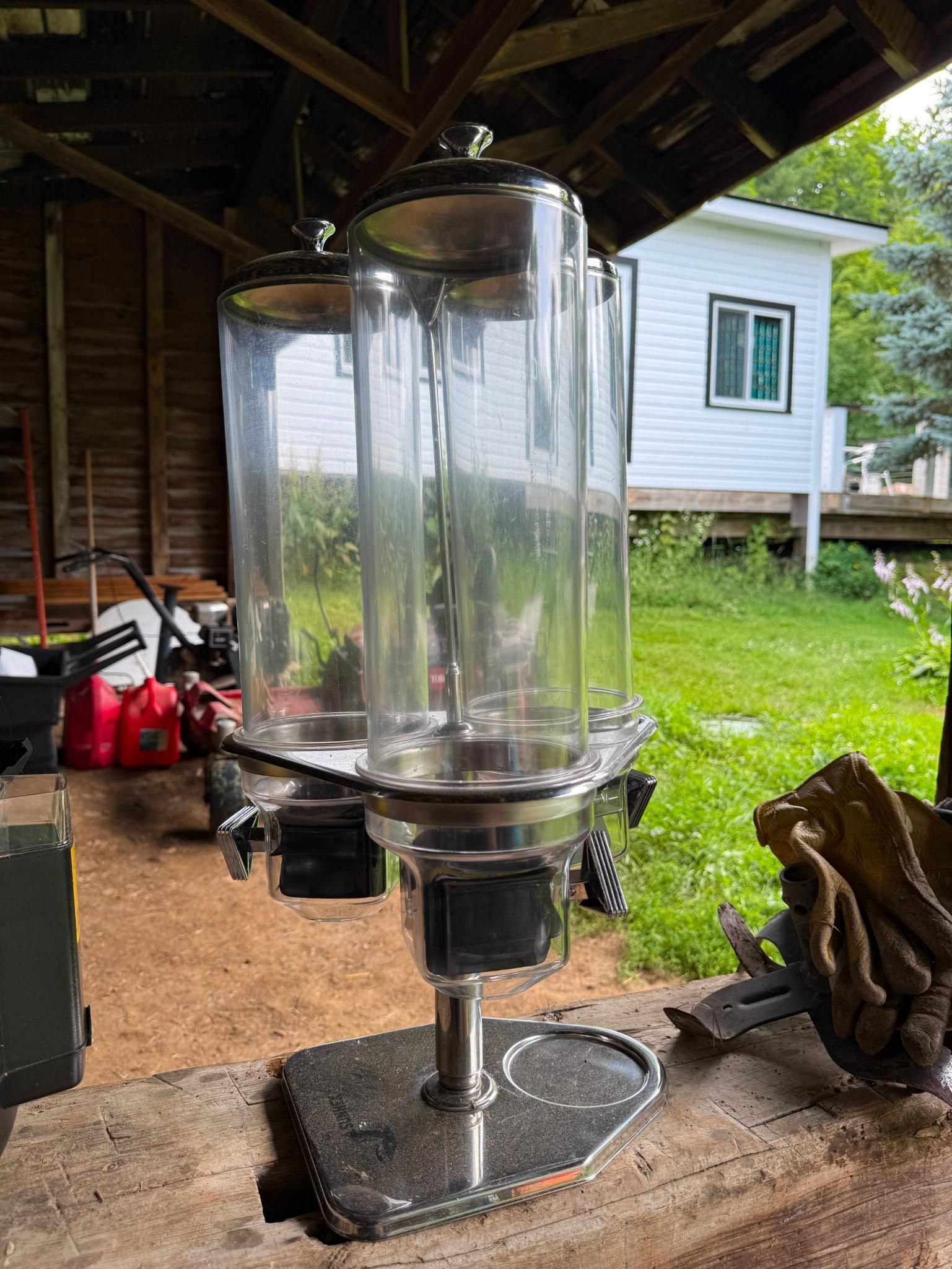 Clear, cylindrical candy dispenser with three canisters on a metal stand.