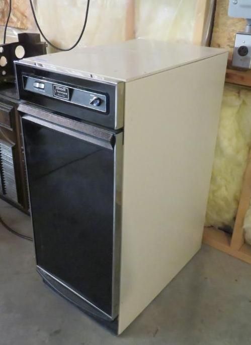 A vintage cream and black refrigerator in a room with a wooden wall.
