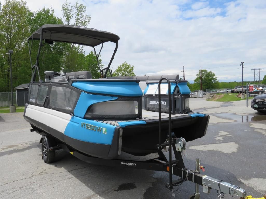 Blue and white pontoon boat on a trailer, black canopy, parked outside on a sunny day.