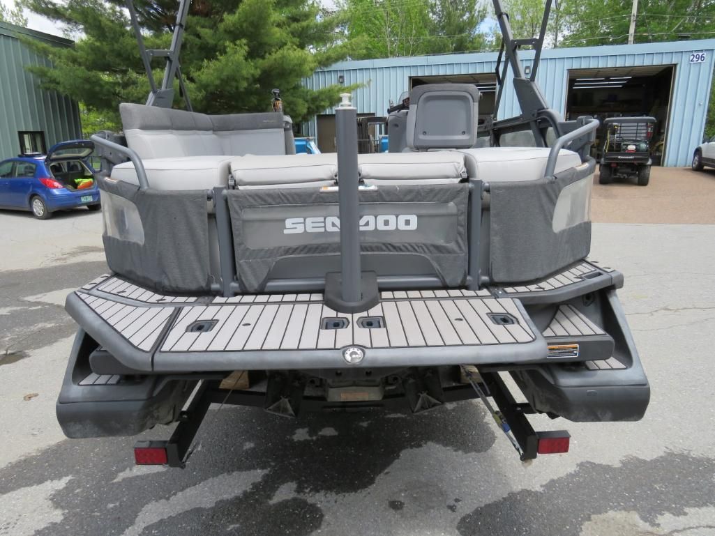 Rear view of a gray Sea-Doo pontoon boat with a textured deck and black accents, parked outside a building.