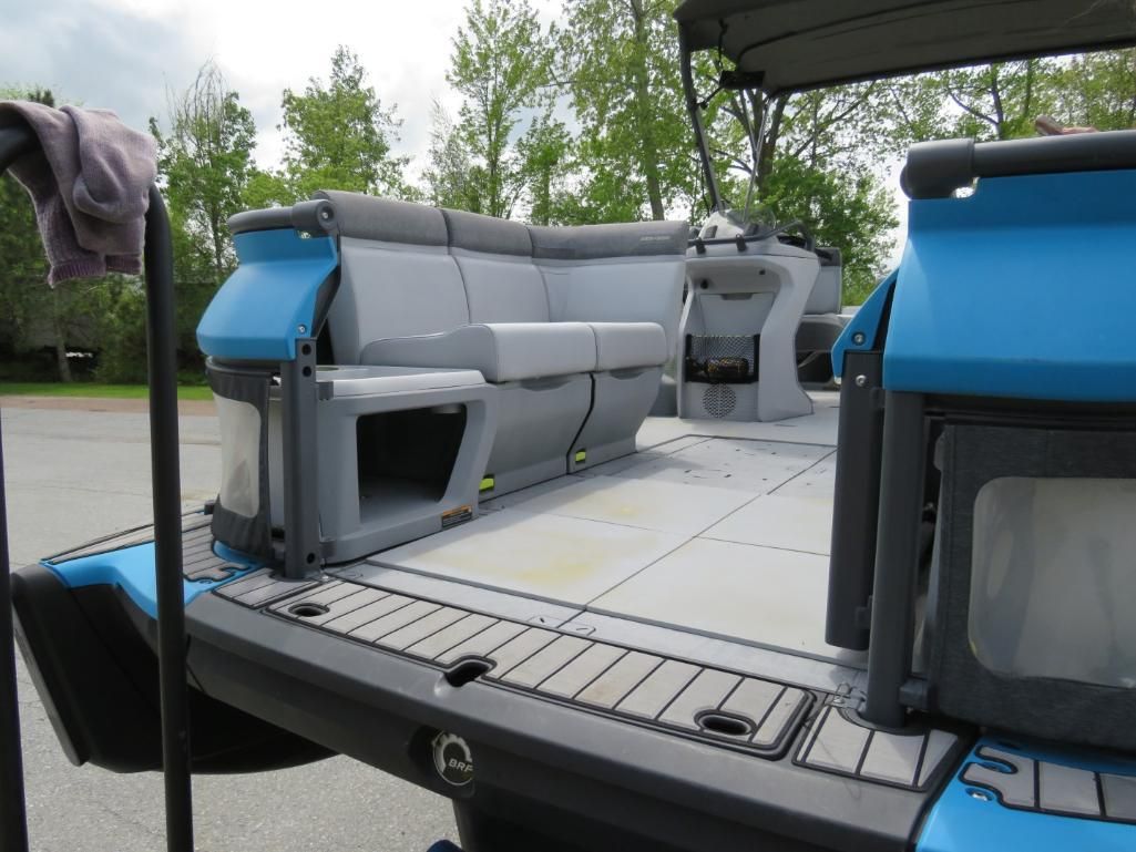A pontoon boat's interior with blue and gray seating, black flooring, and a canopy.