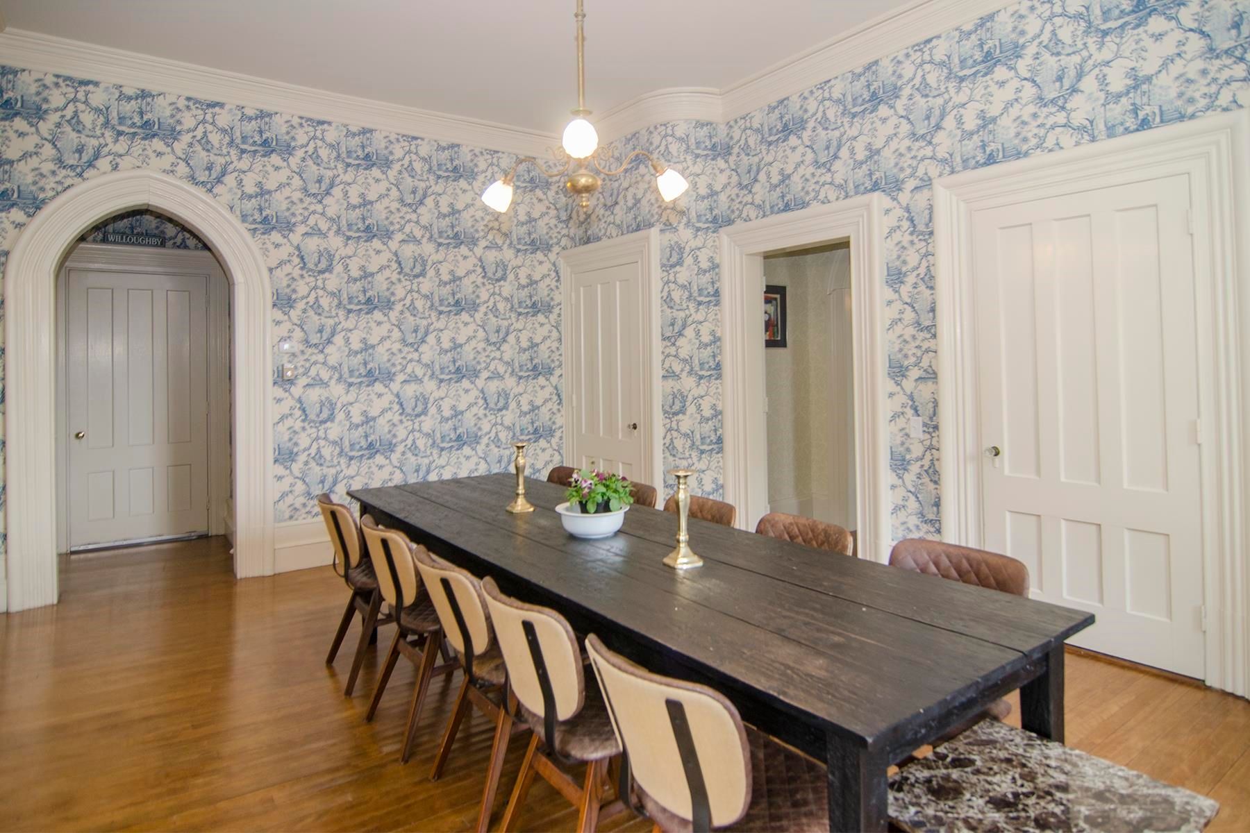 Dining room with long black table, blue patterned wallpaper, and light wood floors.