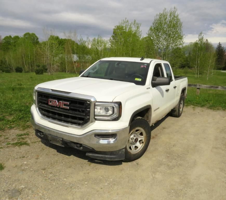 White GMC Sierra pickup truck parked on gravel. Green grass and trees in the background.