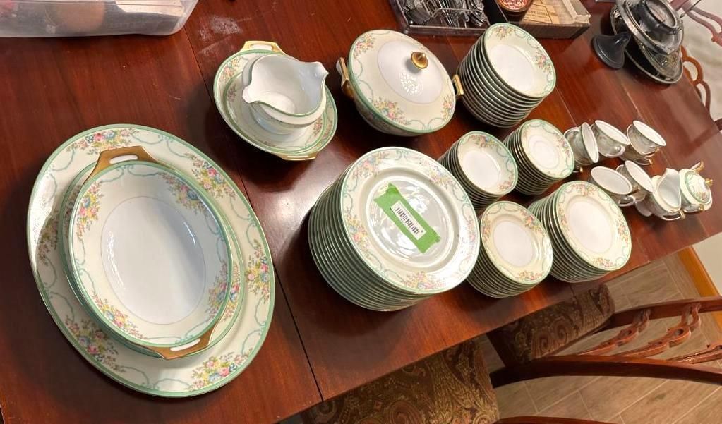 Assortment of antique china dishes, mostly green and gold, on a wooden table.