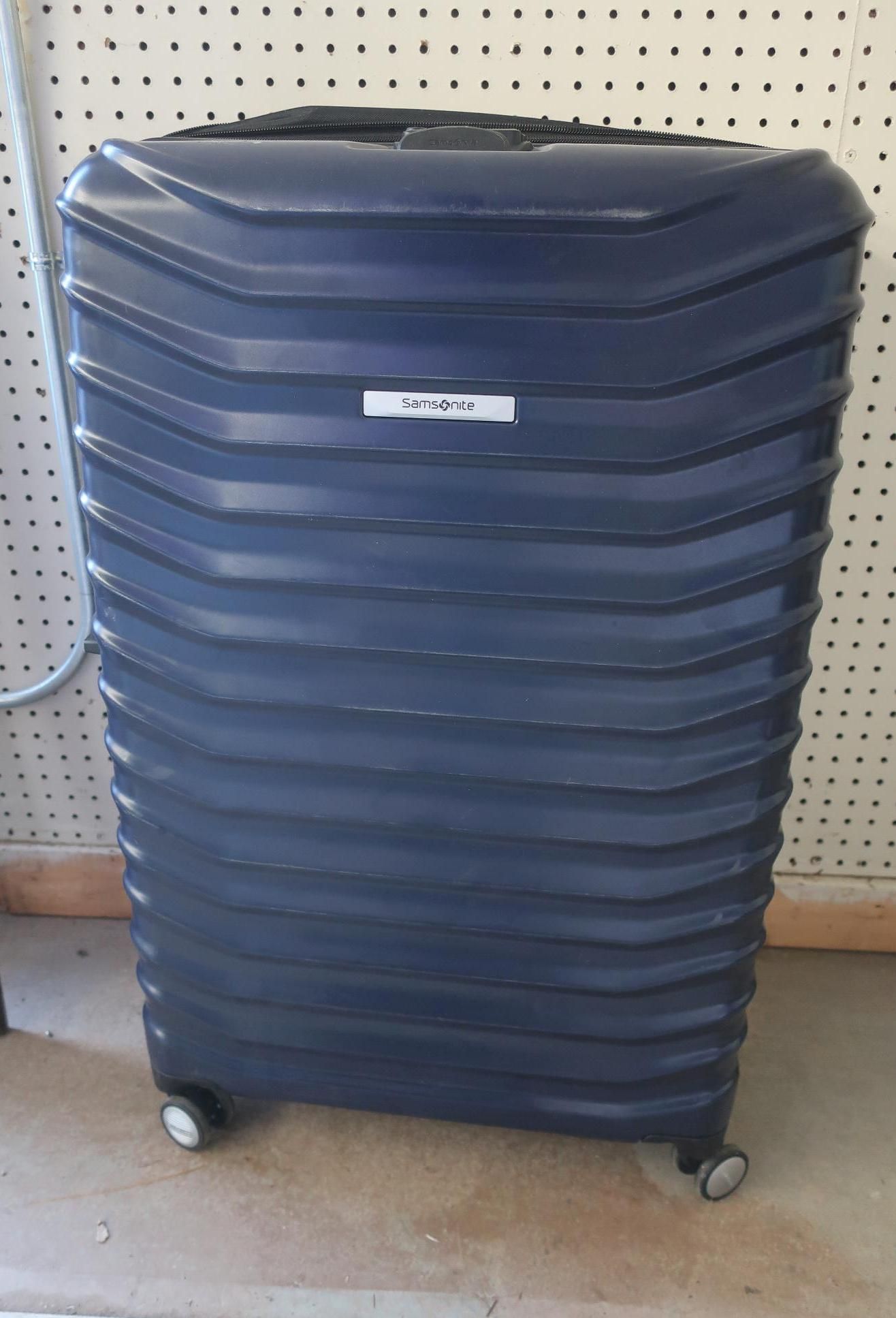 Blue hard-shell suitcase with ridged design, wheels, and a small name tag, indoors.