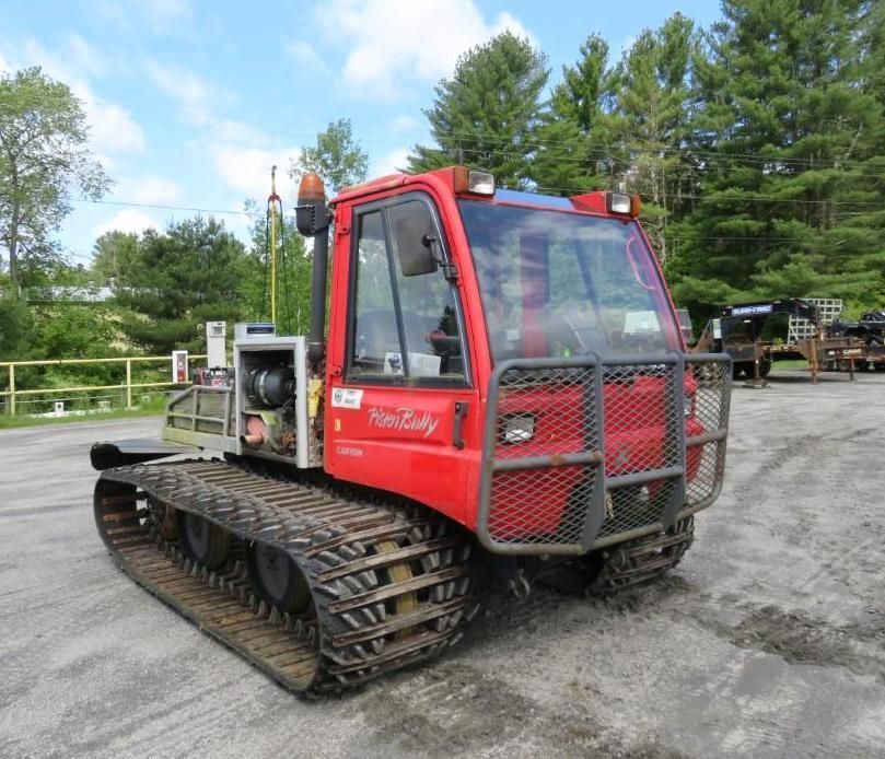 Red Prinoth snow grooming machine on tracks, parked outdoors on asphalt.