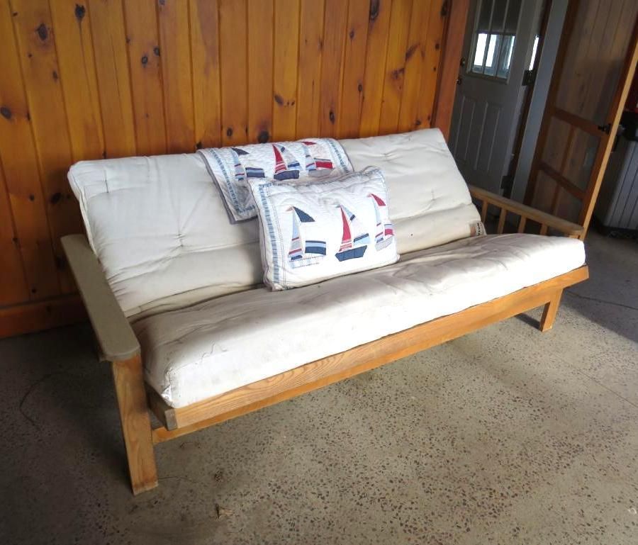 Wooden futon with cream cushions and nautical pillows, set against a wood panel wall.