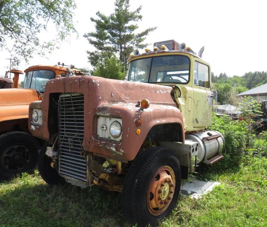 Yellow Mack truck in a grassy lot.