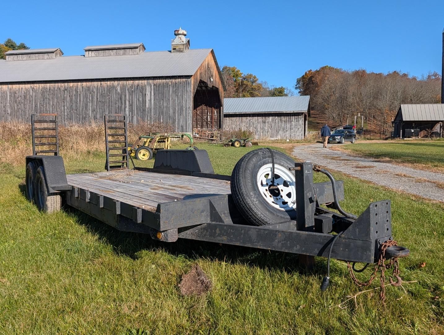 Flatbed trailer parked on grass in a farmyard with barns in the background