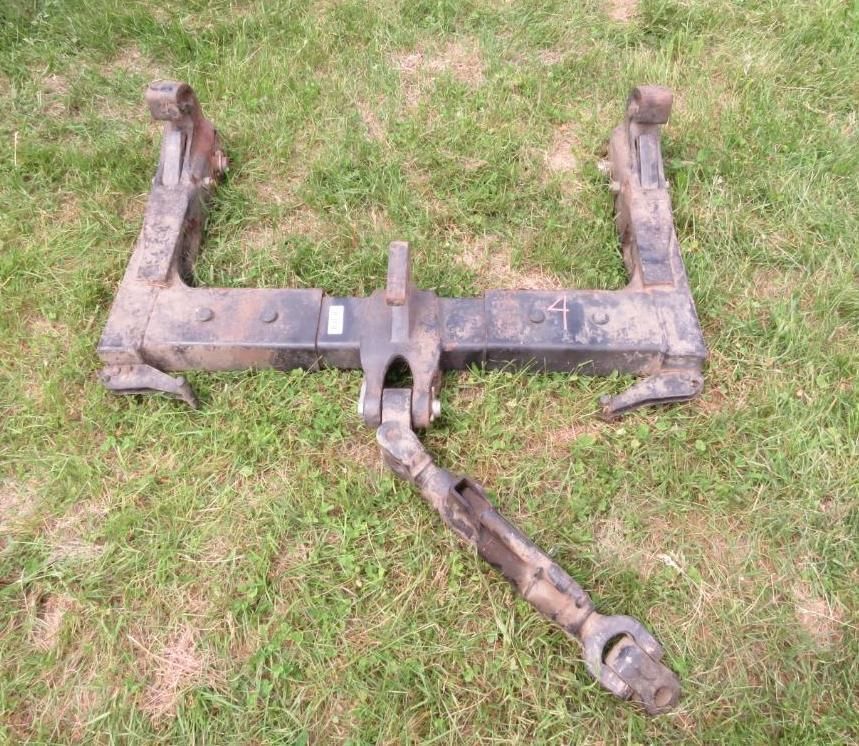 Black tractor three-point hitch with adjustable center link, lying on green grass.