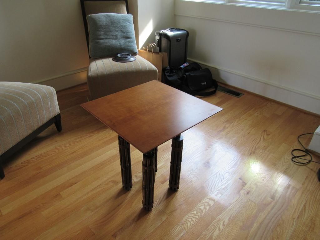A square wooden side table with dark legs in a room with hardwood floors.