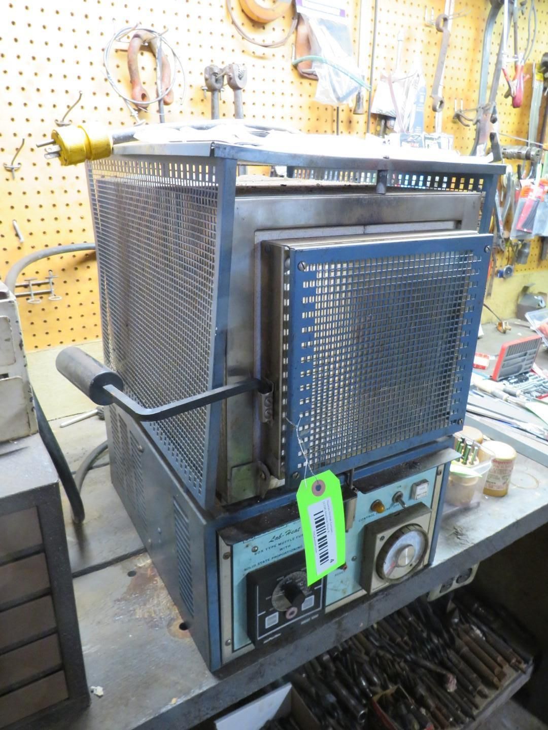 Blue and metal kiln with a mesh exterior and open door, sitting on a work table.