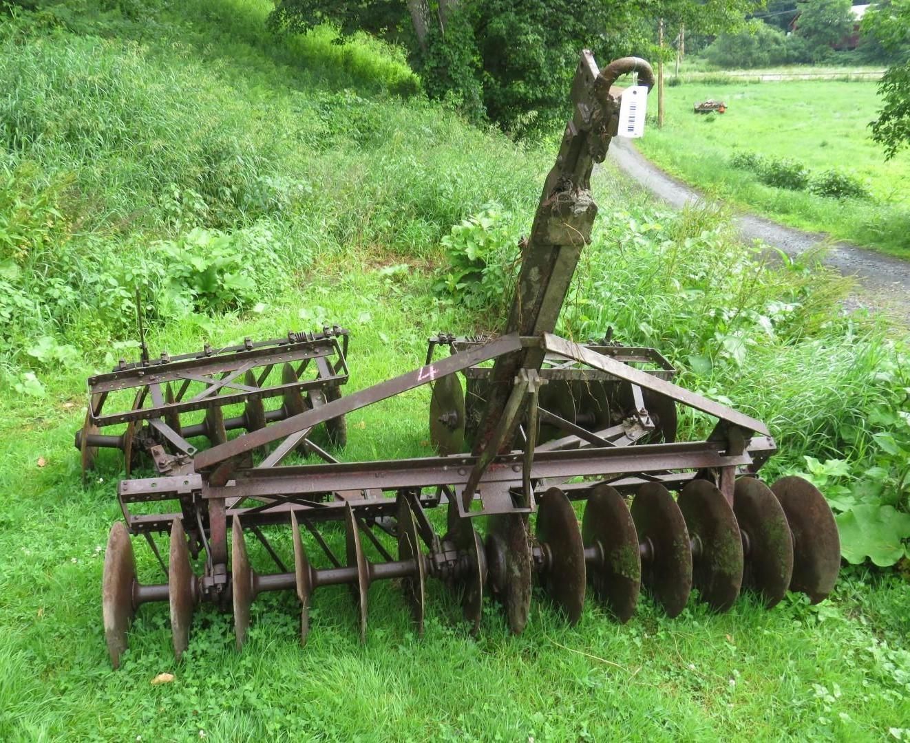 Rusty agricultural disc harrow sitting in grassy field.