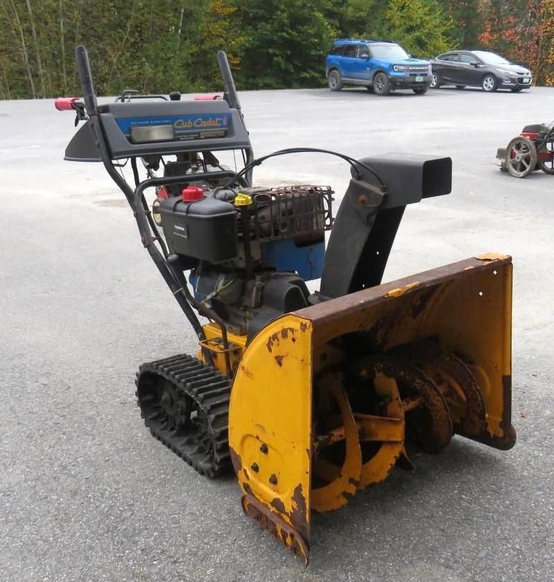 Yellow and black Cub Cadet snowblower with tracks, outdoors.