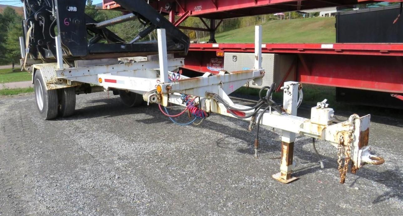 A white utility trailer with a rusty appearance parked on gravel; connected to a larger red trailer.