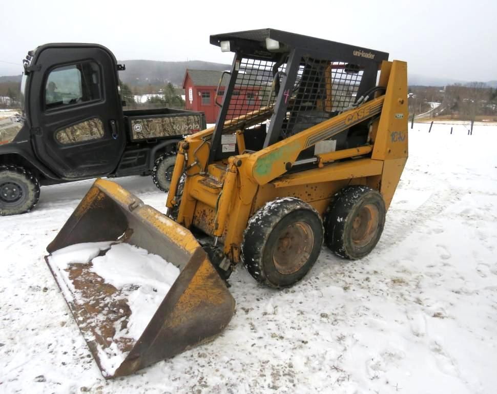 Yellow skid steer loader with bucket in a snowy field.