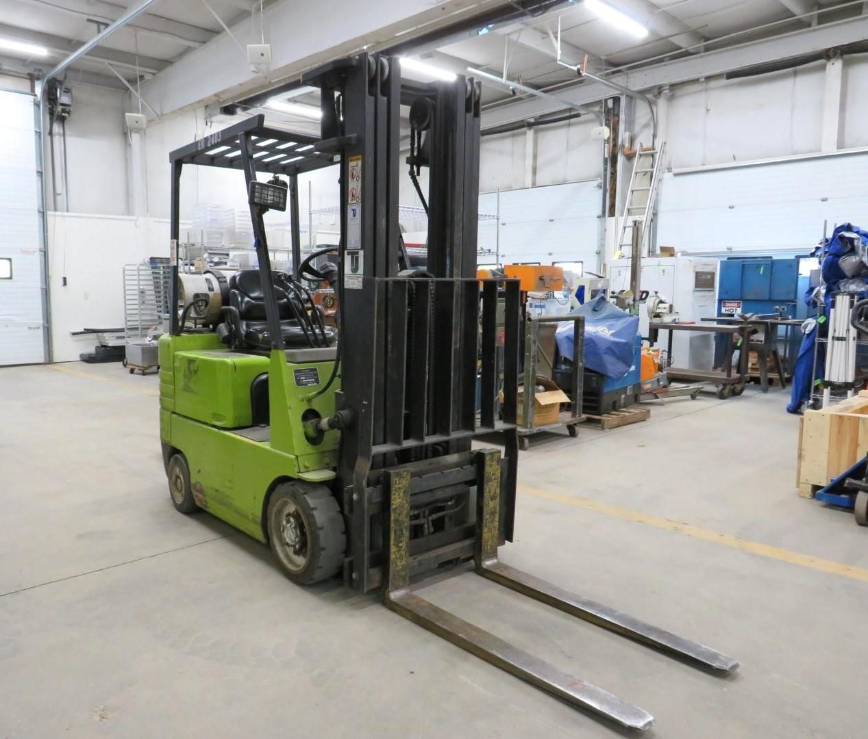Green forklift in a warehouse setting, front view.