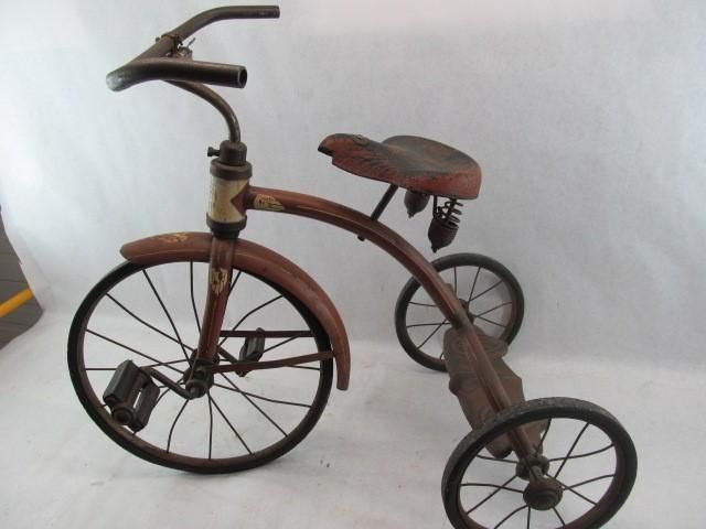 Vintage tricycle with metal frame, brown seat, and small wheels.