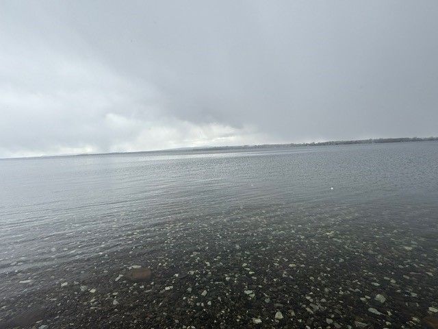 Calm, gray water under an overcast sky. Rocky shoreline in the foreground.