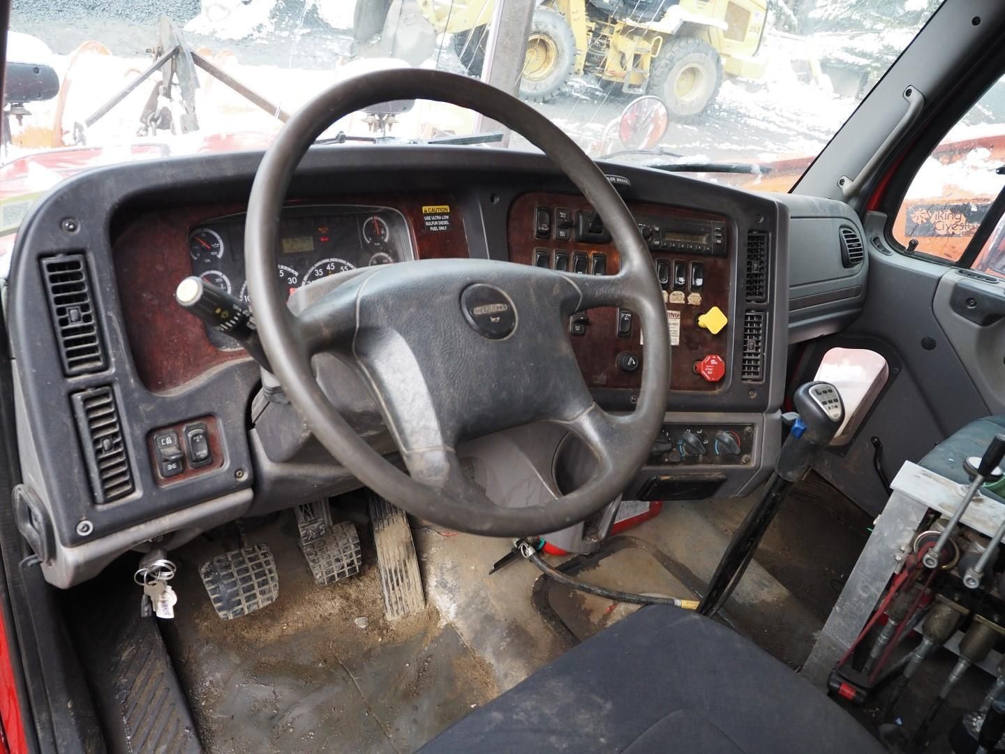 Truck cab interior with steering wheel, gauges, and pedals. Red dashboard, black wheel.