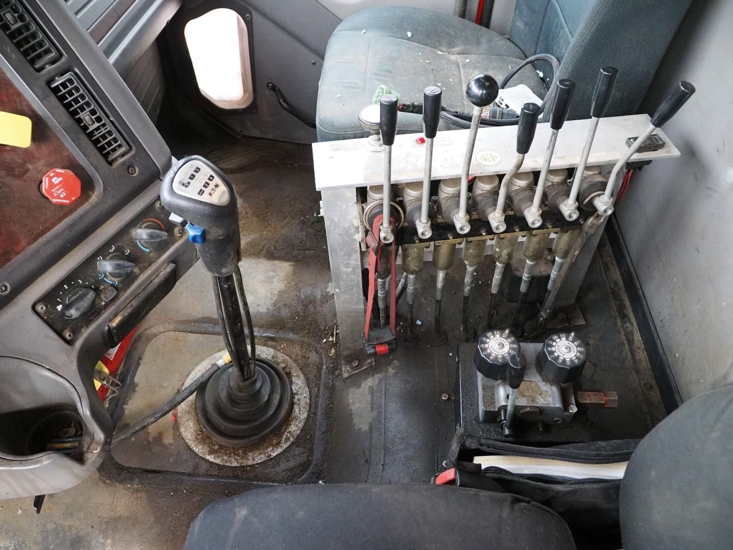 Interior of a truck cab, showing a gear shift lever, levers for operating equipment, and control knobs.