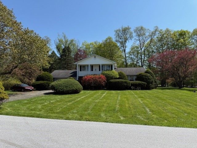 House with white siding and a well-manicured lawn and trees on a sunny day.
