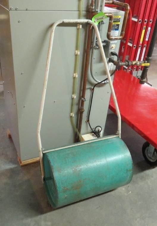 Green lawn roller with white handle, in a utility room setting.