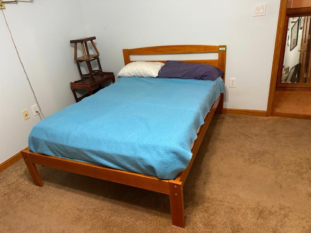 Wooden bed frame with blue bedding, pillows, and a chair in a room with brown carpet.