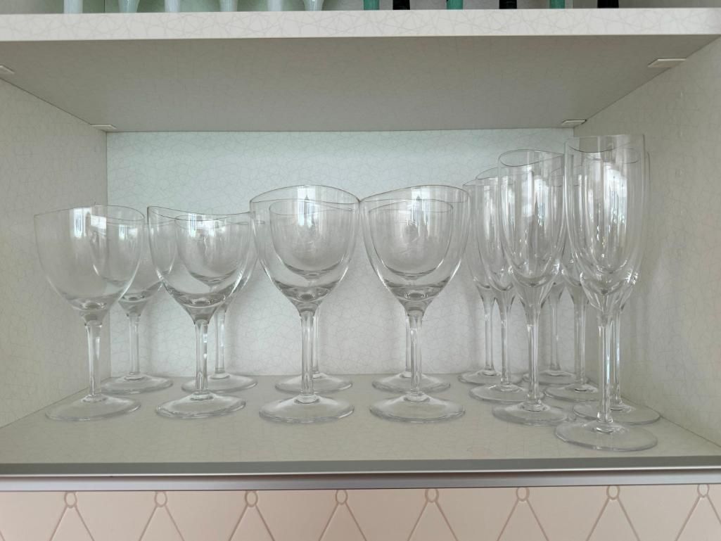Clear wine glasses are arranged on a shelf.