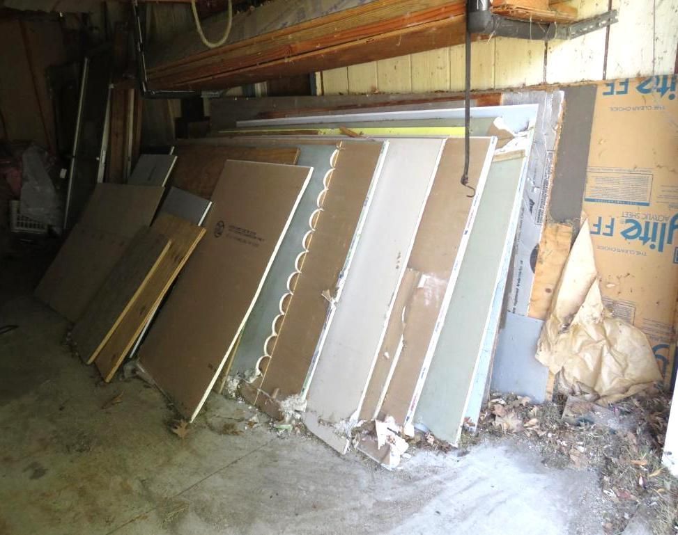 Pile of drywall sheets leaning against a wall in a garage.