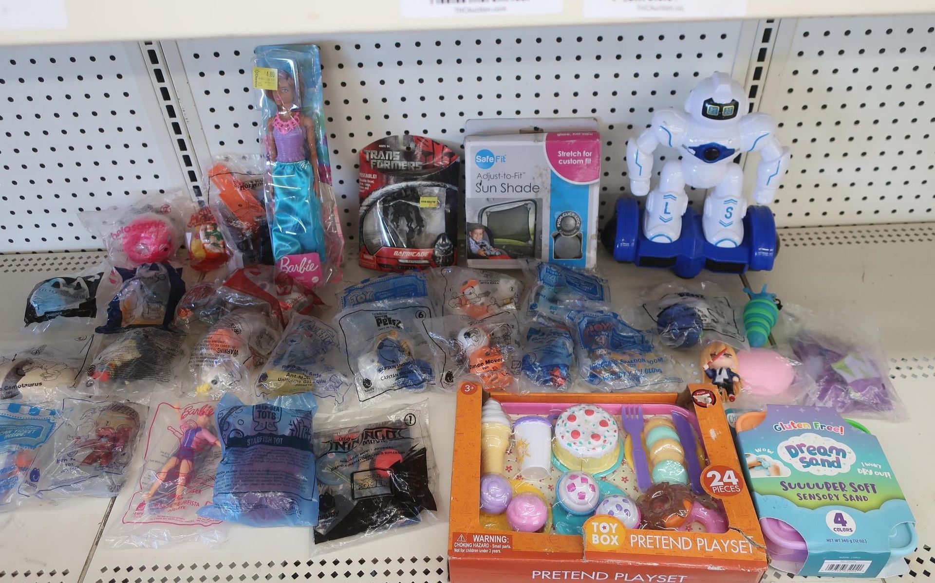 Toys on a store shelf, including a robot, doll, and food play set.