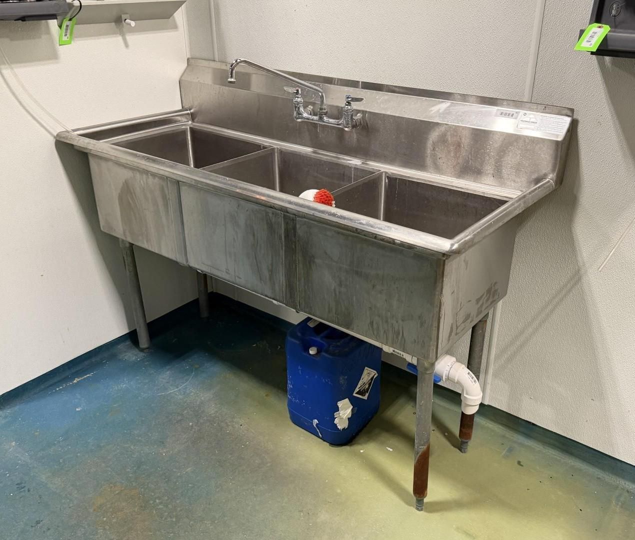 Stainless steel three-basin sink in a commercial kitchen setting.