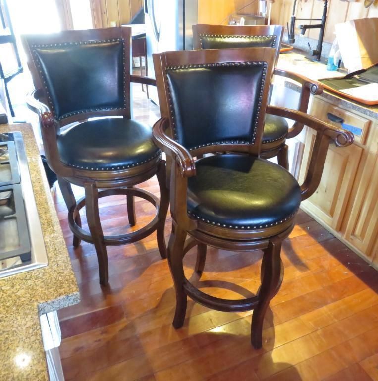 Three brown wooden bar stools with black leather seats in a kitchen.