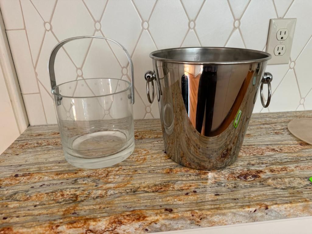 Clear glass bucket and stainless steel ice bucket on a granite countertop.