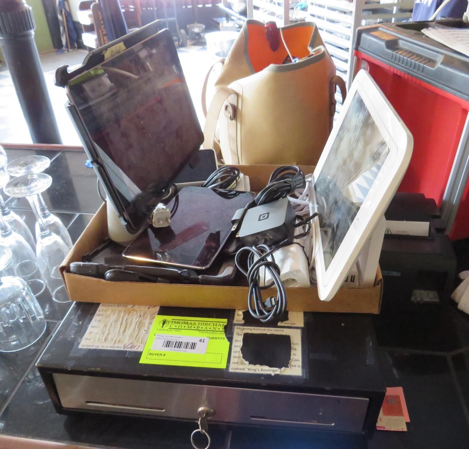 Cash register setup with tablets, bag, and receipt printer on a counter.
