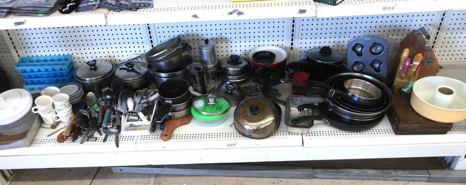 Kitchenware display on a shelf at a store, featuring pots, pans, utensils, cups, and baking molds.