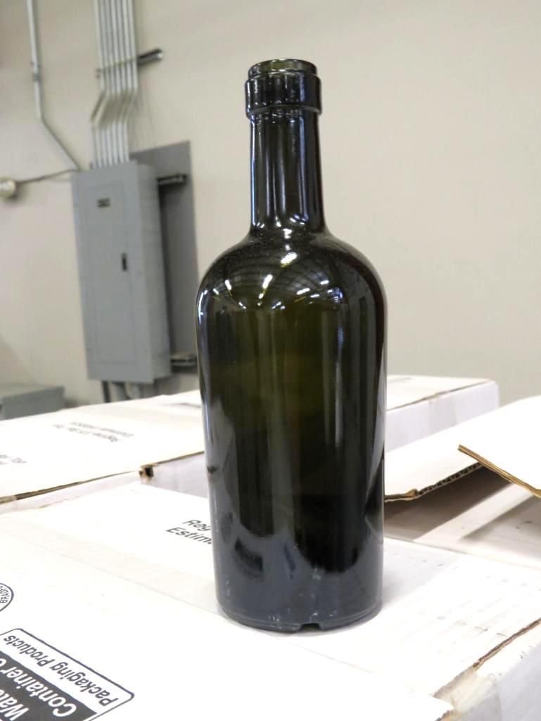 Green glass wine bottle on a stack of cardboard boxes, in an industrial setting.