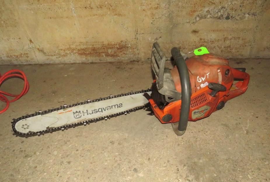 Husqvarna chainsaw on concrete floor, orange and silver, against a wall.