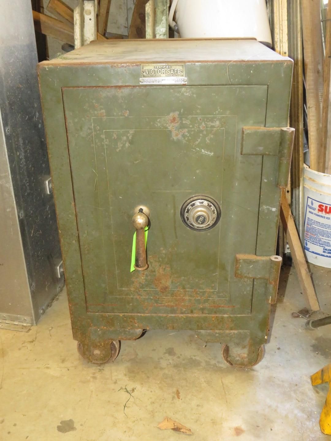 Old, green metal safe with combination dial, handle, and wheels.