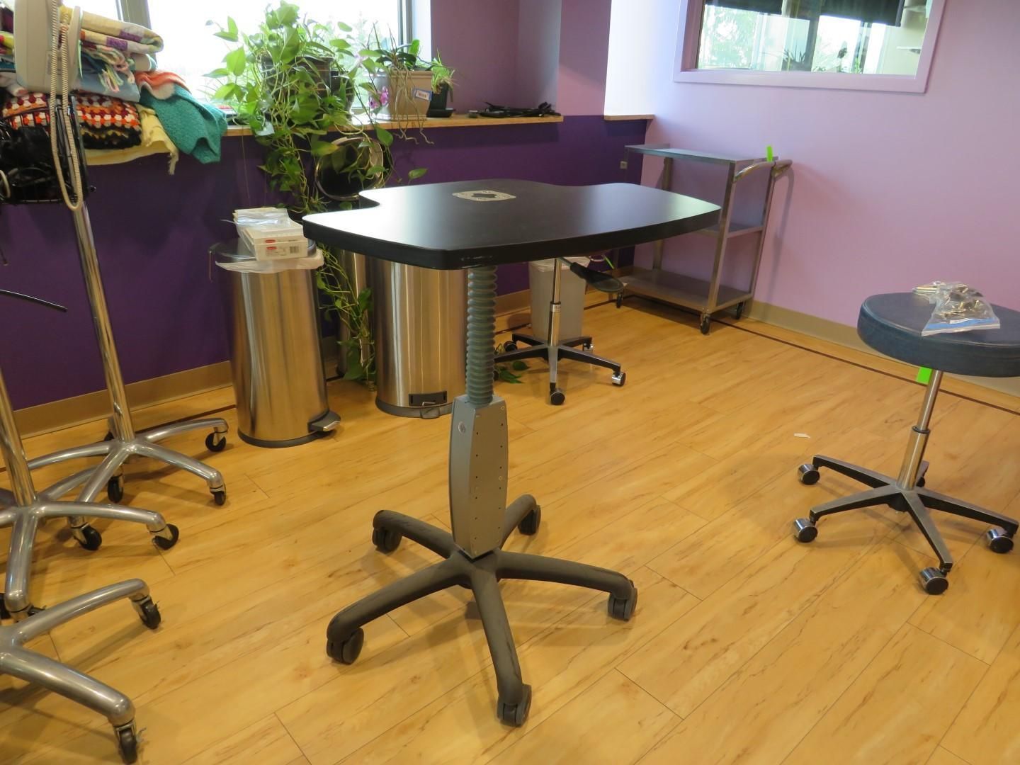 Black adjustable height table on wheels in a room with hardwood floors.