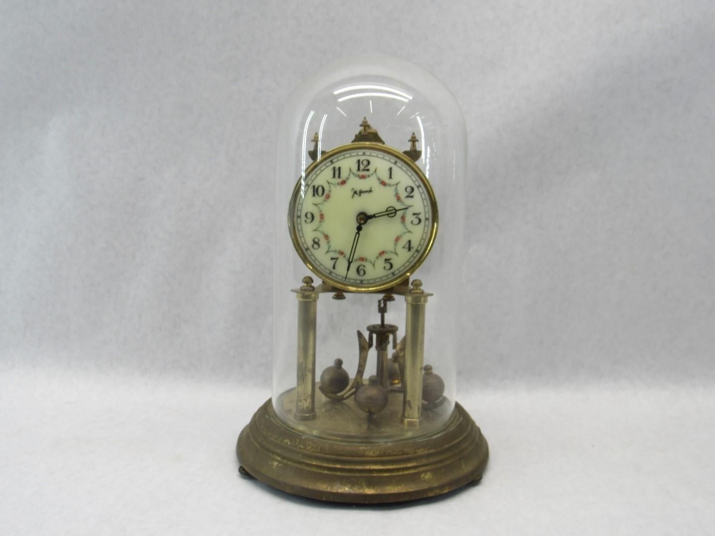 Antique clock with pendulum inside a glass dome on a brass base.