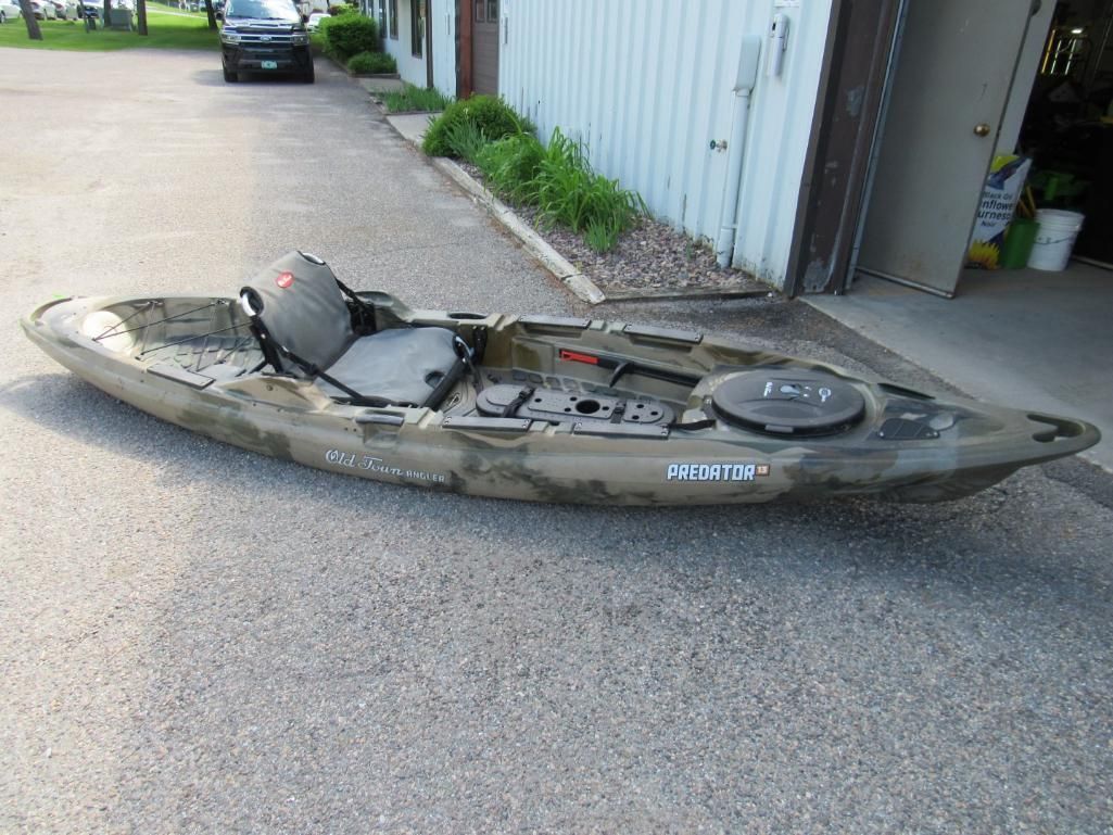 Camouflage kayak on asphalt in front of a building.