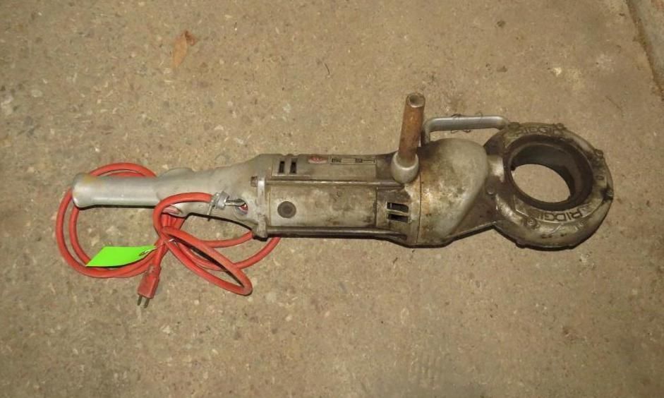 Electric pipe threader with a red cord, resting on a concrete surface.