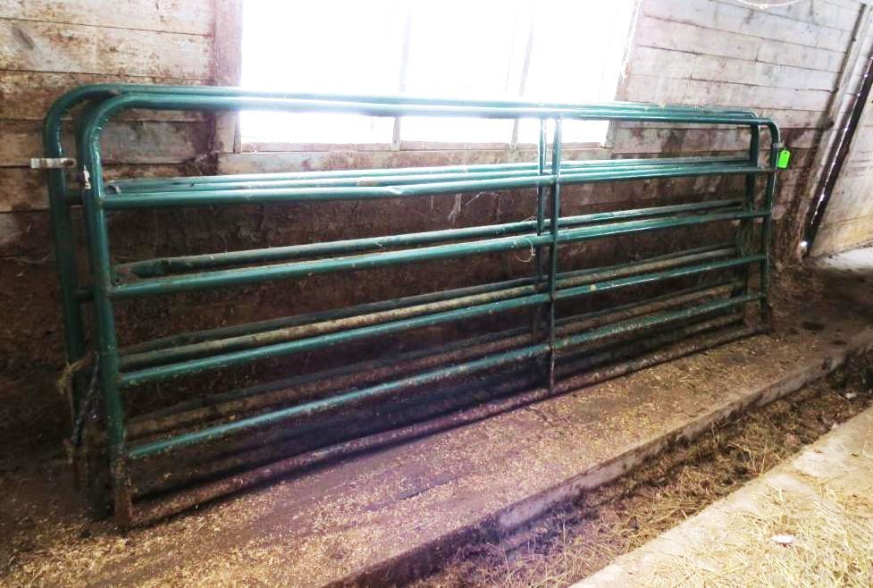 Green metal farm gates stacked inside a barn.