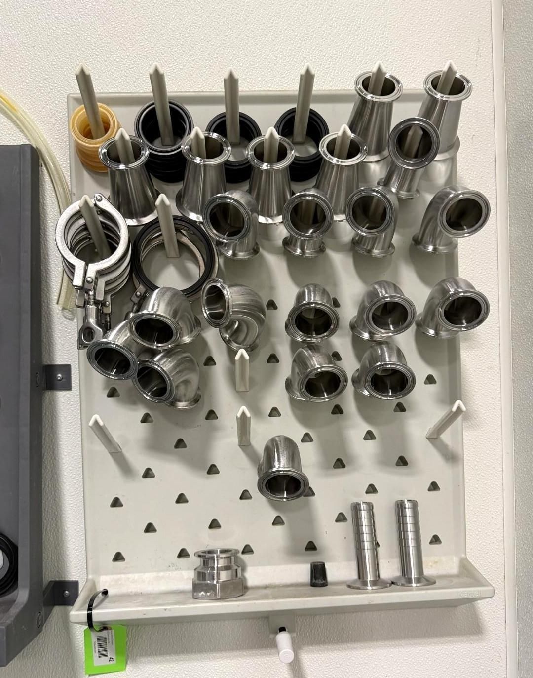 Stainless steel pipe fittings arranged on a pegboard.