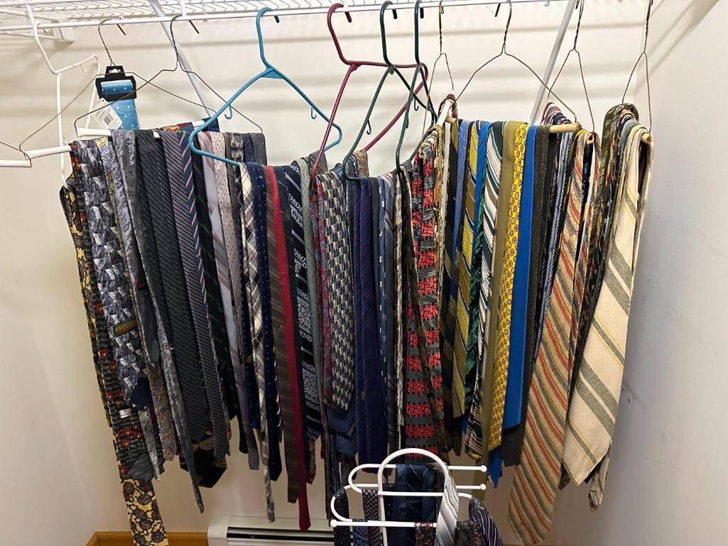 A collection of neckties hanging on wire hangers in a closet.