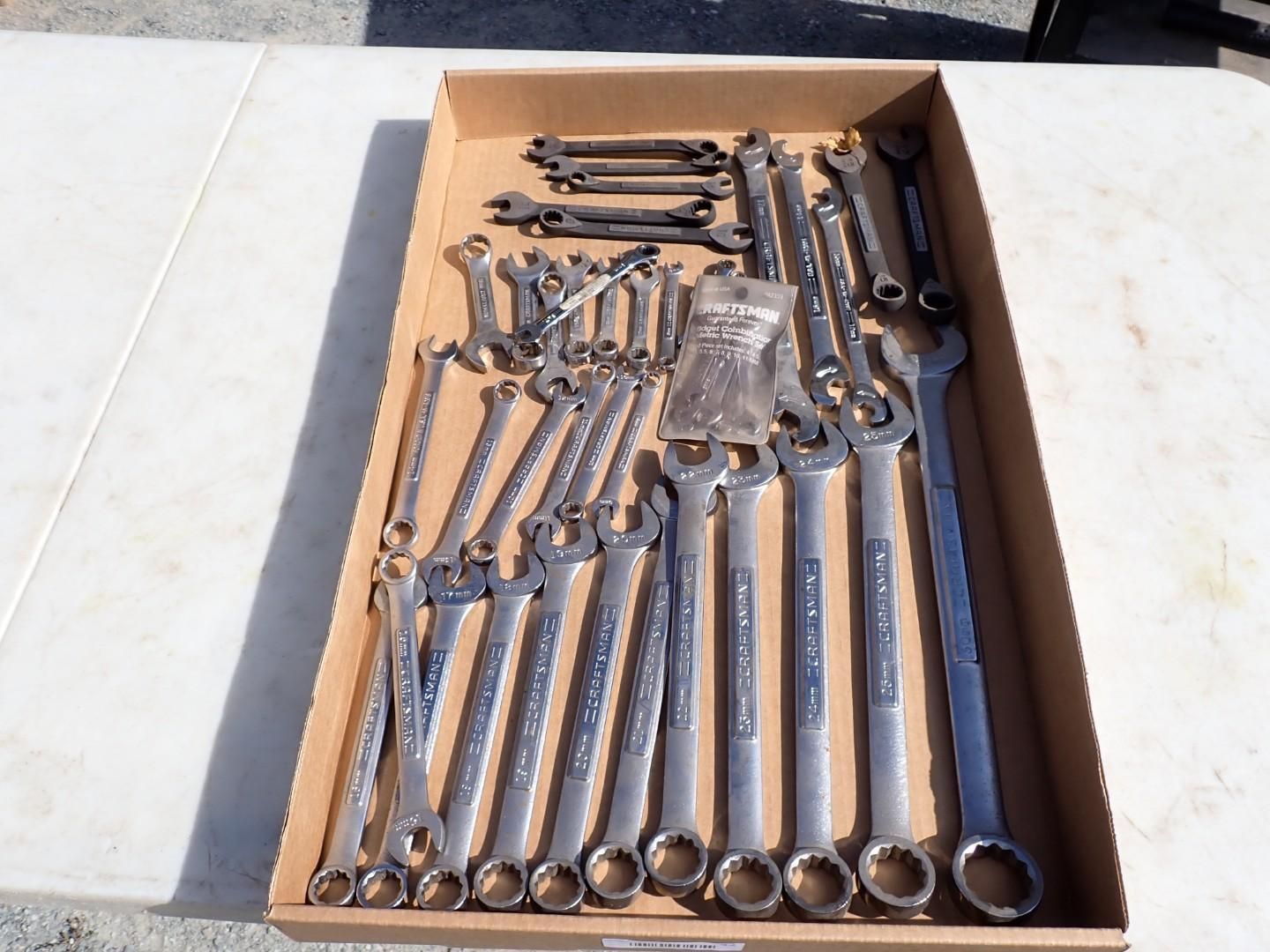 Box of assorted metal wrenches and hand tools laid out on a concrete surface
