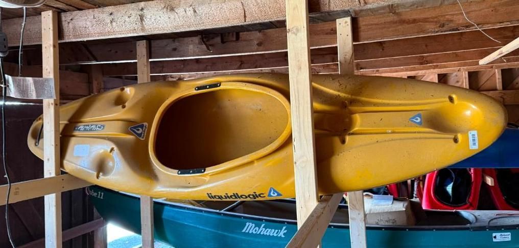 Yellow kayak stored on wooden supports inside a shed with other boats.