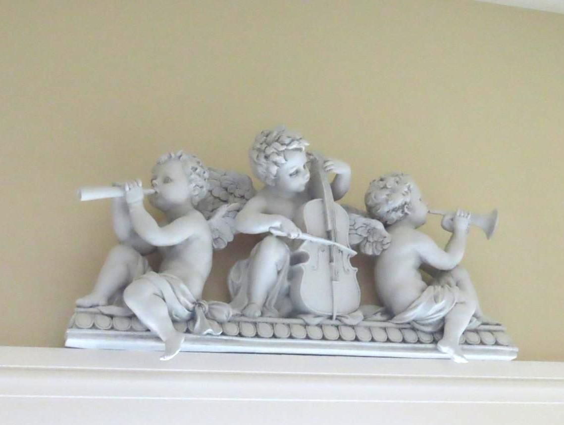 Three cherub statues play musical instruments: flute, cello, trumpet.
